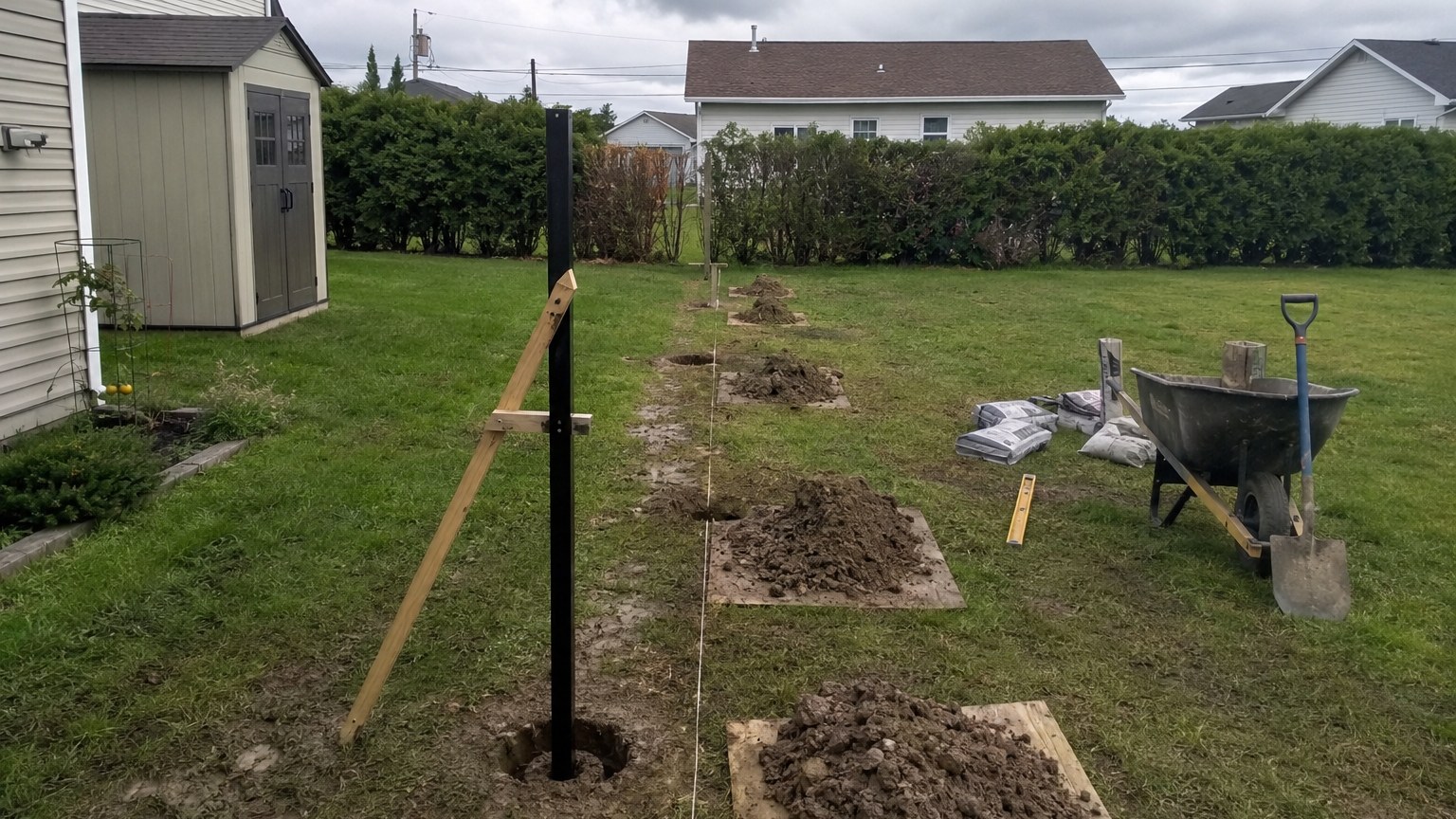String line and augered post holes along a property line between two lawns, the first post centred and plumb in its hole
