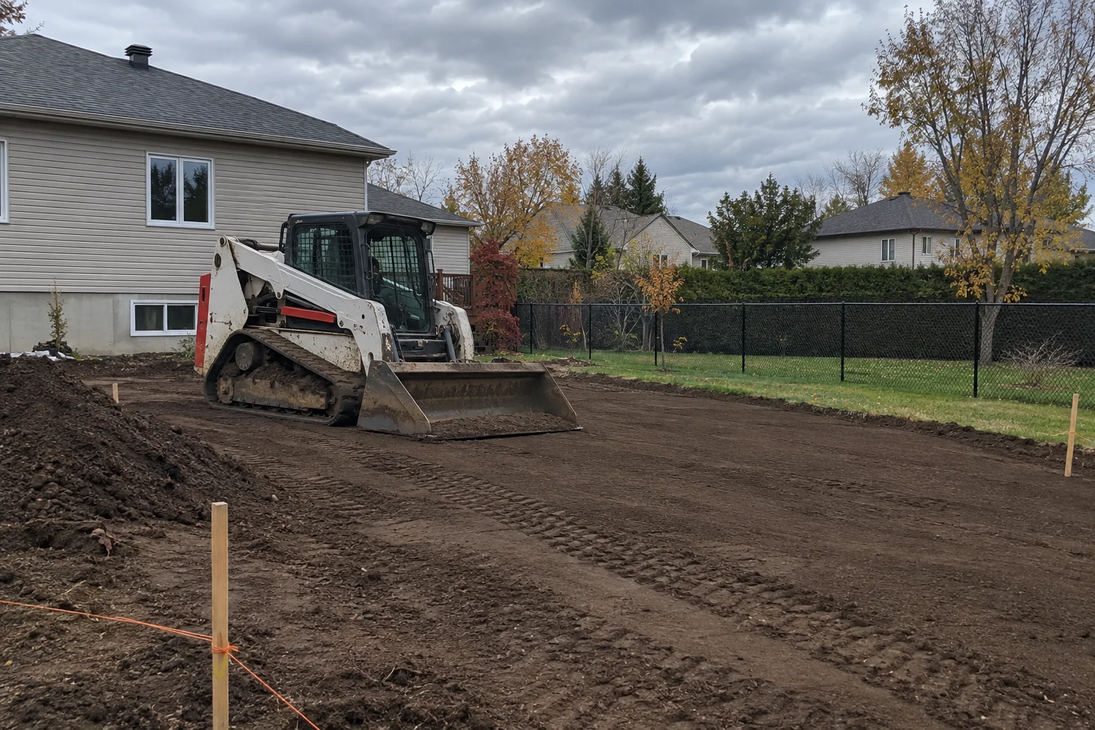 Compact tracked loader fine-grading topsoil so the yard slopes away from the house